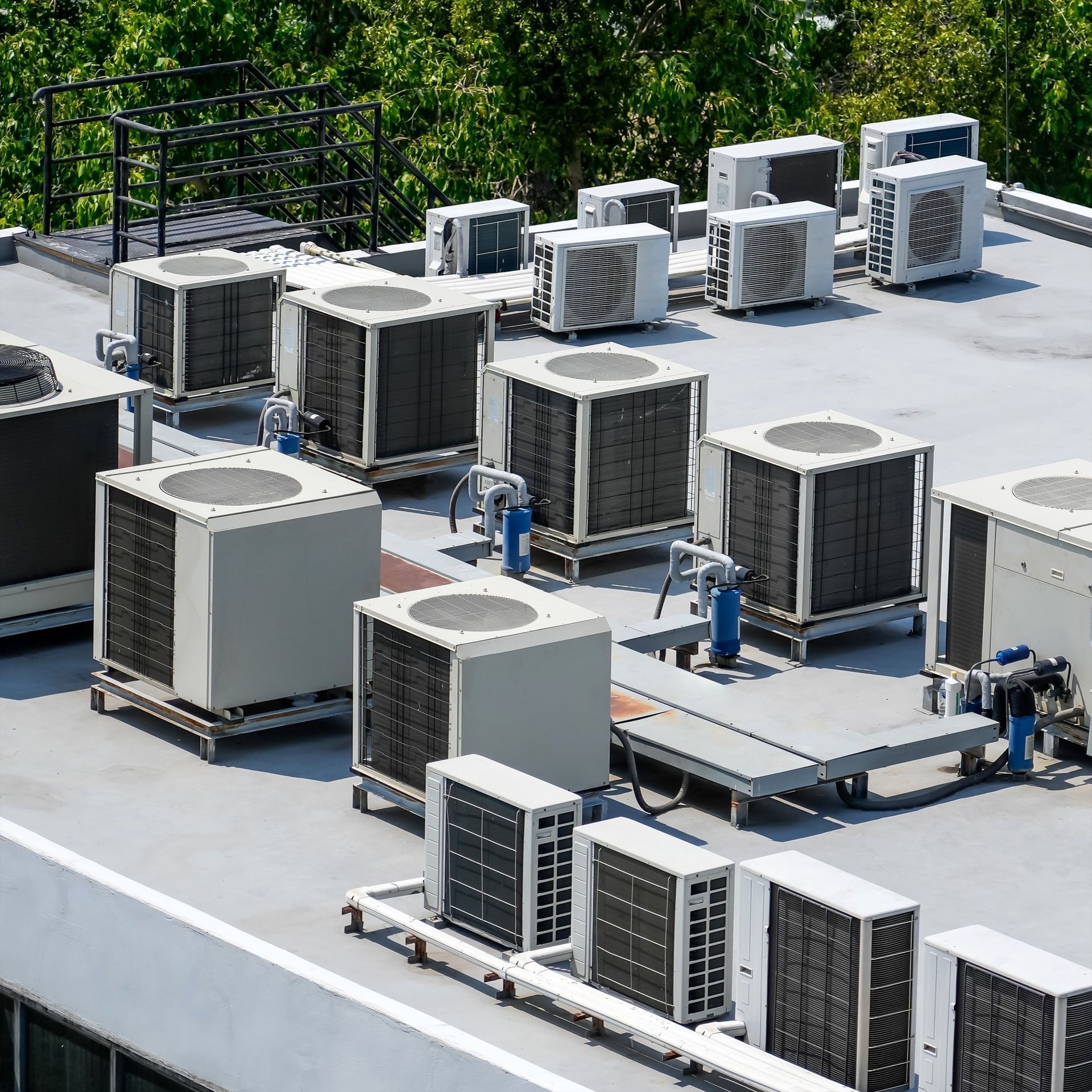 Air conditioning units on a rooftop, white and gray against a concrete surface. Green trees in the background.