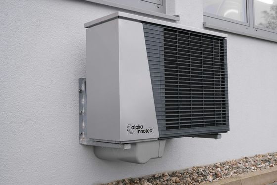 Gray heat pump mounted on a white exterior wall.