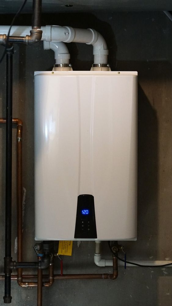White wall-mounted water heater with white PVC exhaust pipes, copper pipes, and a digital display.