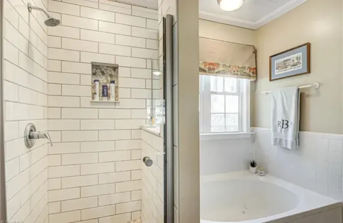 A bathroom featuring a white subway tile shower stall beside a circular soaking tub and a window with a valance.