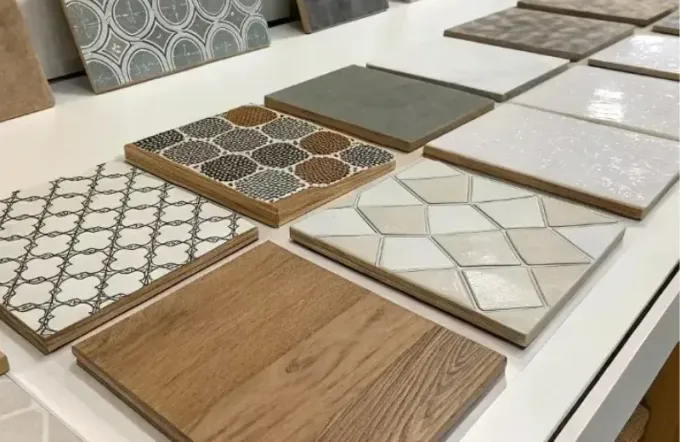 A display of various square floor and wall tile samples in a showroom, featuring wood-look, patterned, and solid styles.