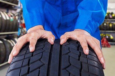 Mechanic Holding a Tire in Vehicle Shop — Wheel Alignments & New Tires in Biddeford, ME Mechanic Holding a Tire in Vehicle Shop — Wheel Alignments & New Tires in Biddeford, ME