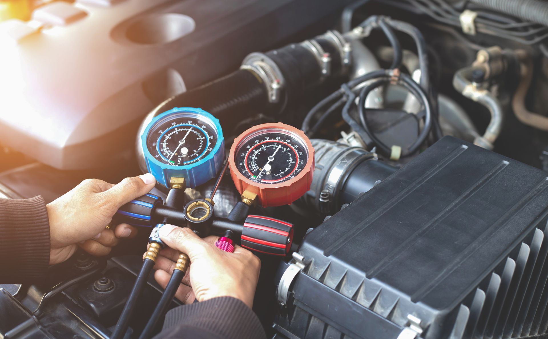 A mechanic using AC pressure gauges to service a car air conditioner.