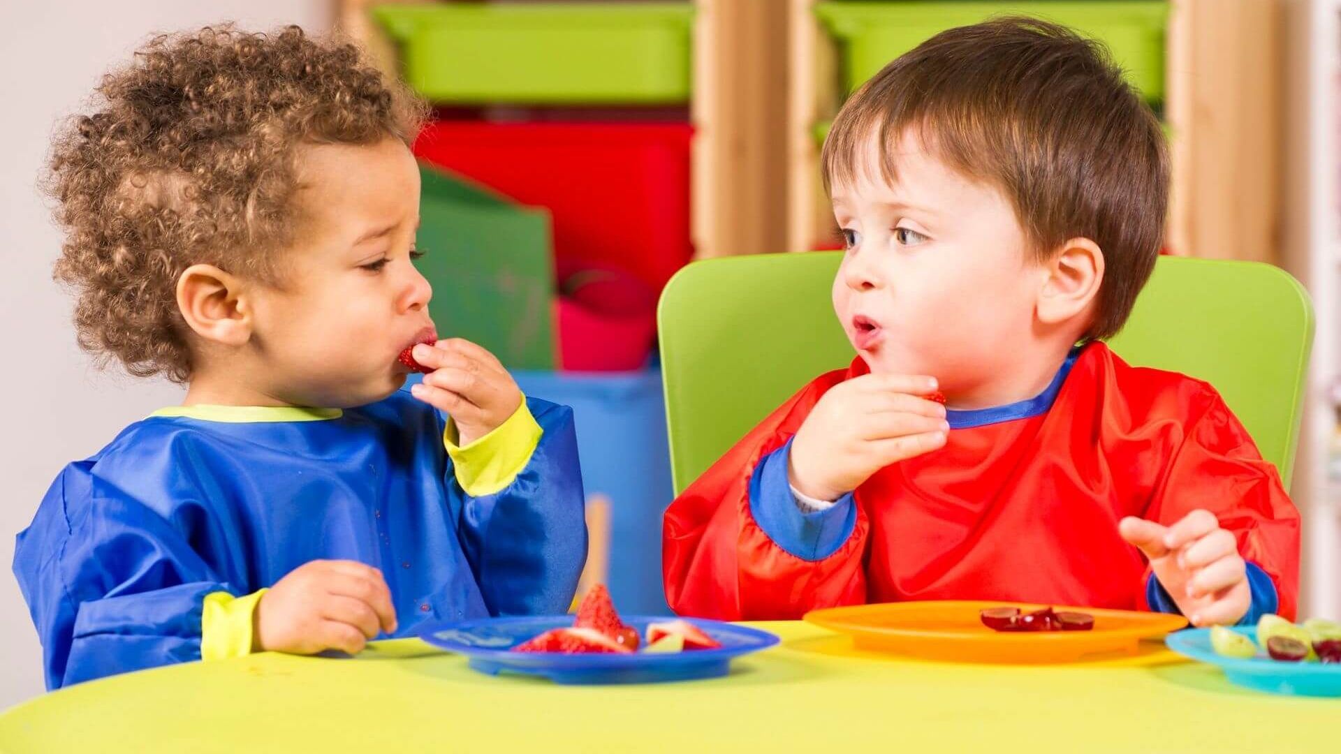 Two young boys are sitting at a table eating from plates.