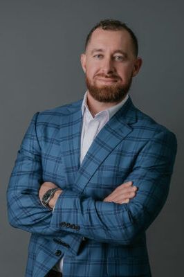 A man in a blue plaid suit is standing with his arms crossed.