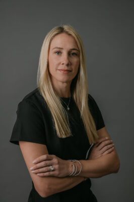 A woman in a black shirt is standing with her arms crossed.