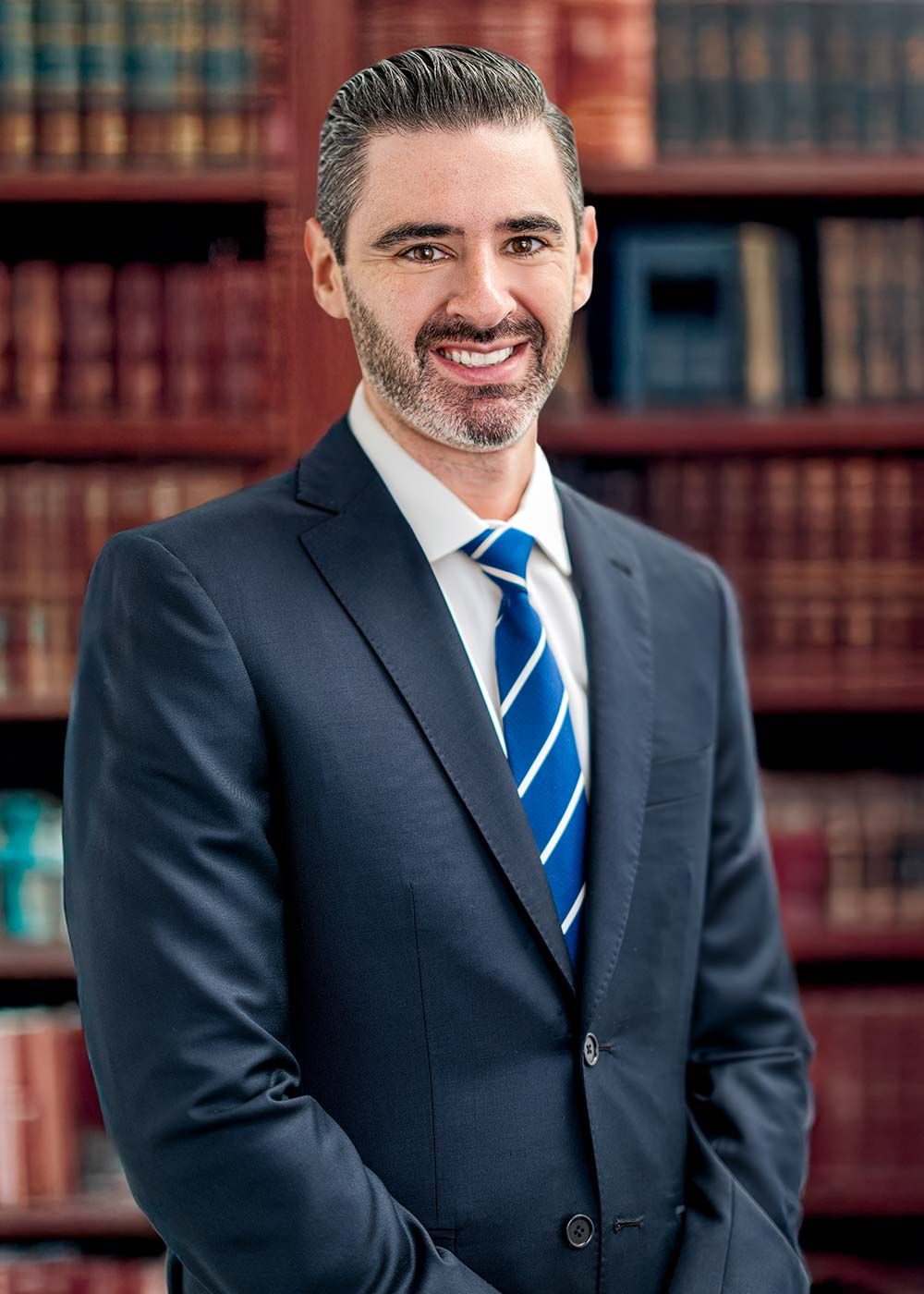 A man in a suit and tie is standing in front of a bookshelf.
