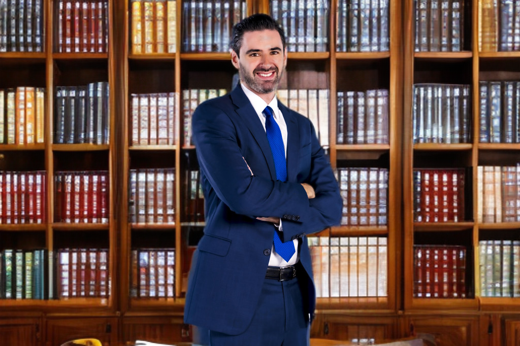 A man in a suit and tie is standing in front of a bookshelf.