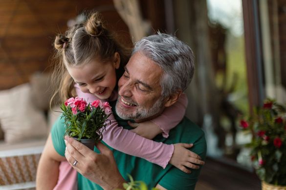 A little girl is holding a potted plant and hugging her grandfather.