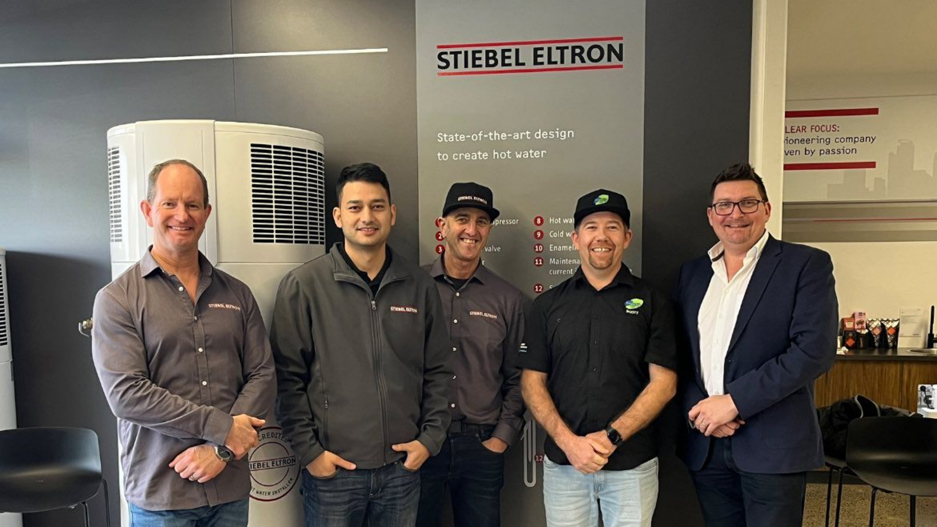 Five people standing in front of a wall with a Stiebel Eltron logo. They appear to be indoors, possibly a showroom.