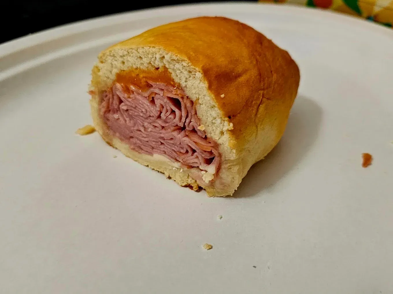 Half of a sandwich on a white plate; filled with ham and sauce, with golden-brown bread.