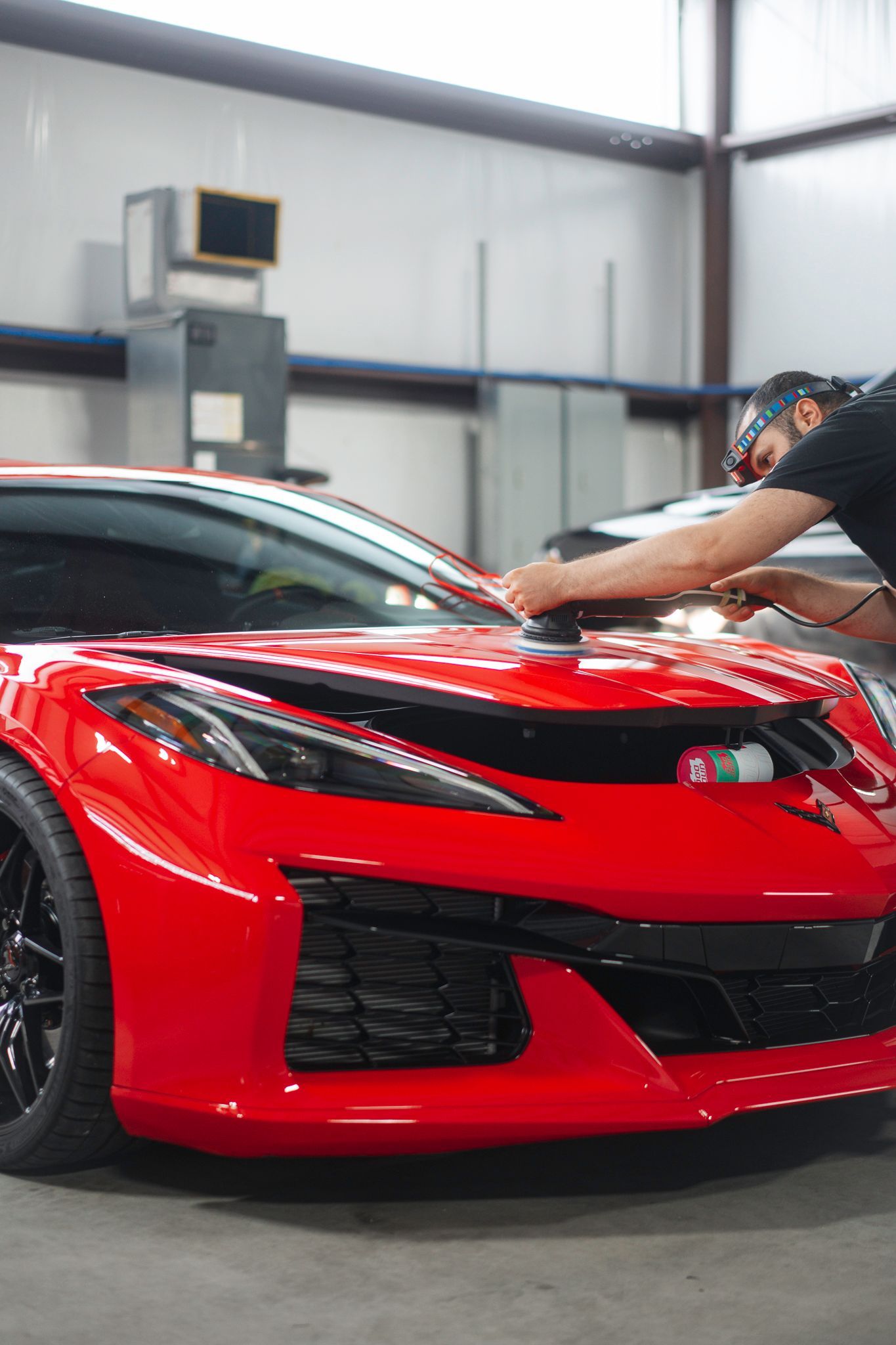 A man is polishing a red sports car in a garage.