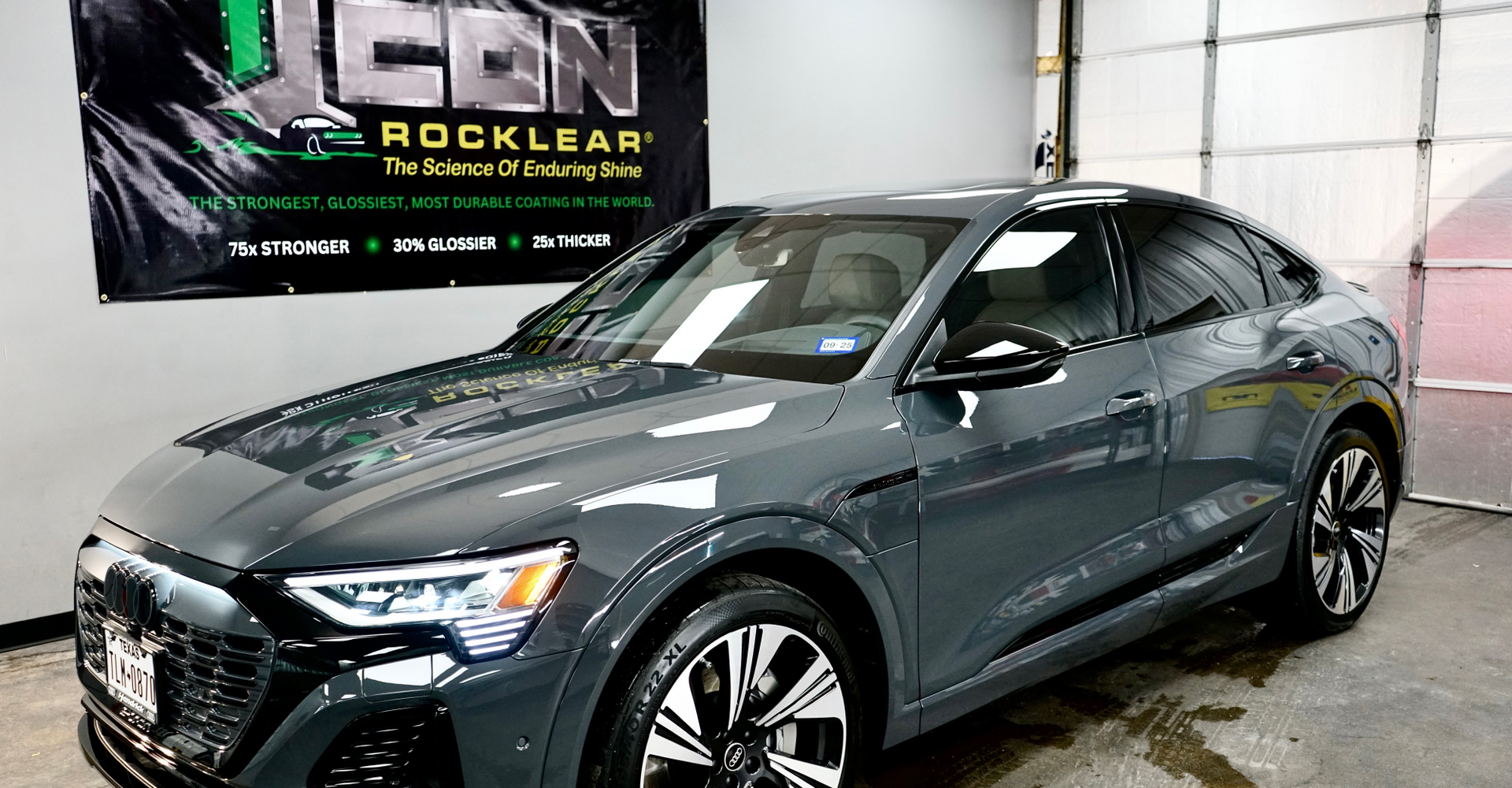 A gray audi e-tron is parked in front of a garage door.