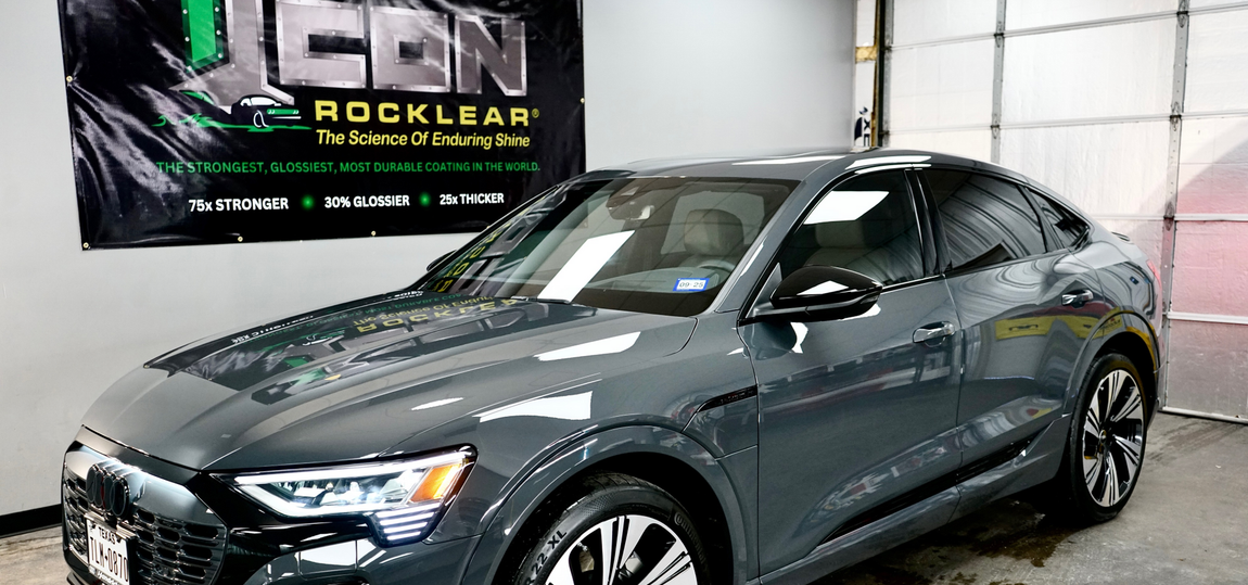 A gray audi e-tron is parked in front of a garage door.