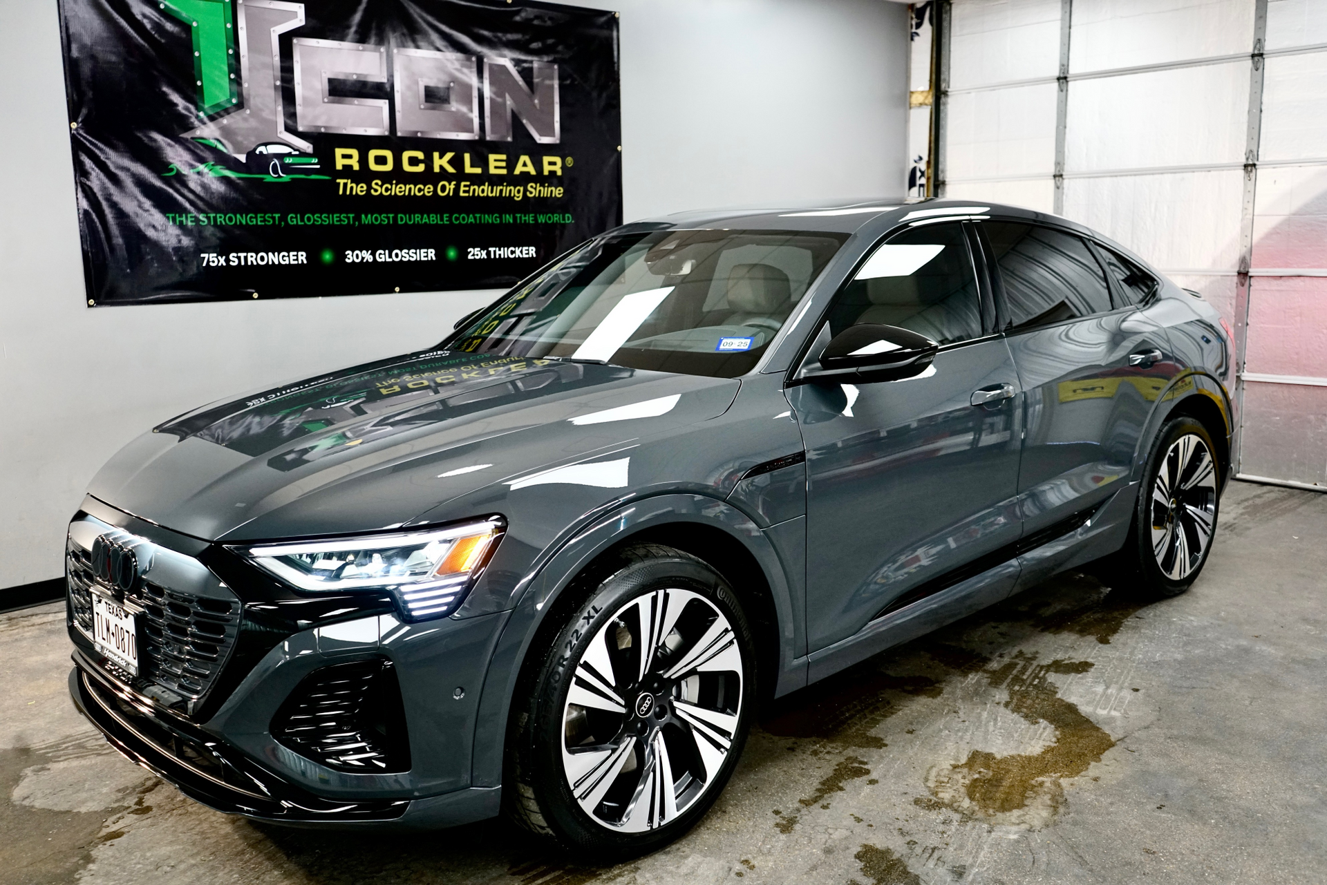 A gray audi e-tron is parked in front of a garage door.