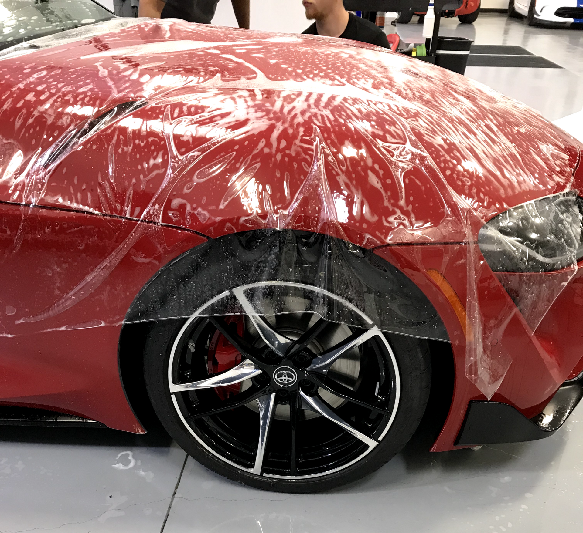 A red sports car is wrapped in clear plastic