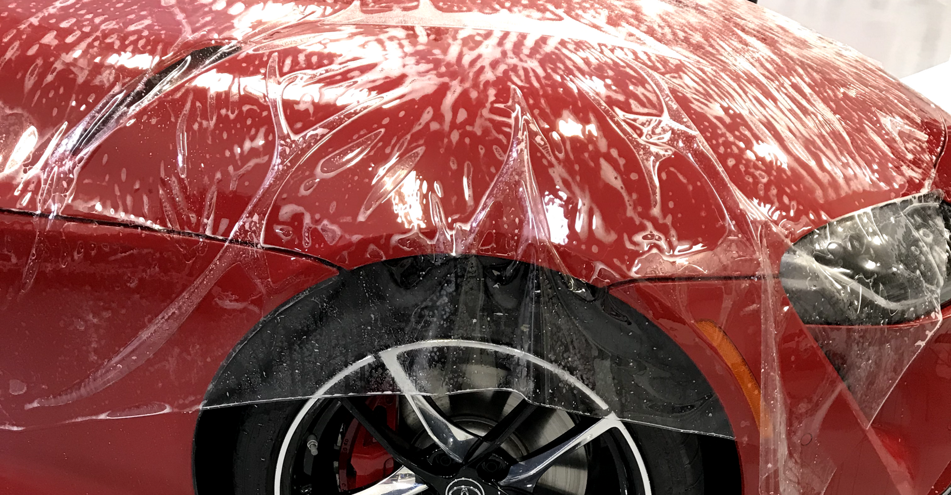 A red car is covered in plastic wrap.