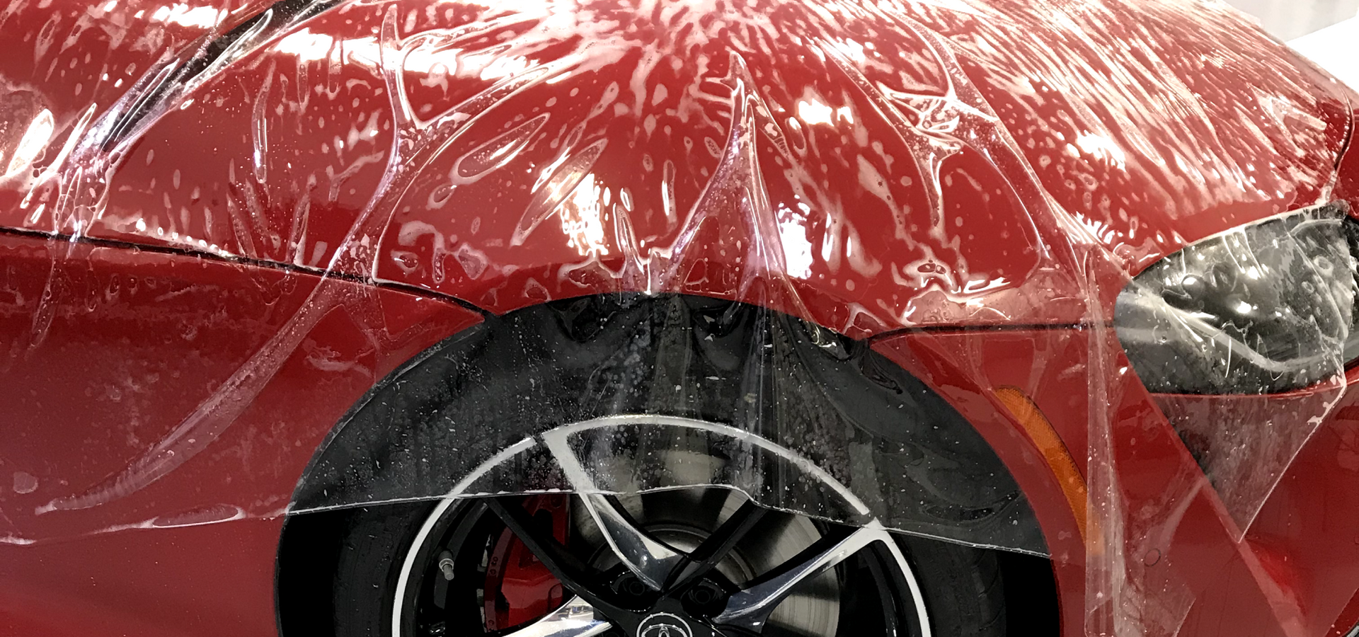 A red car is covered in plastic wrap.