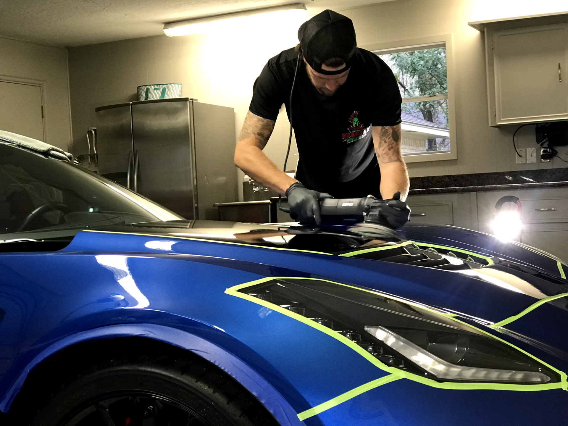 A man is polishing a blue car in a garage.
