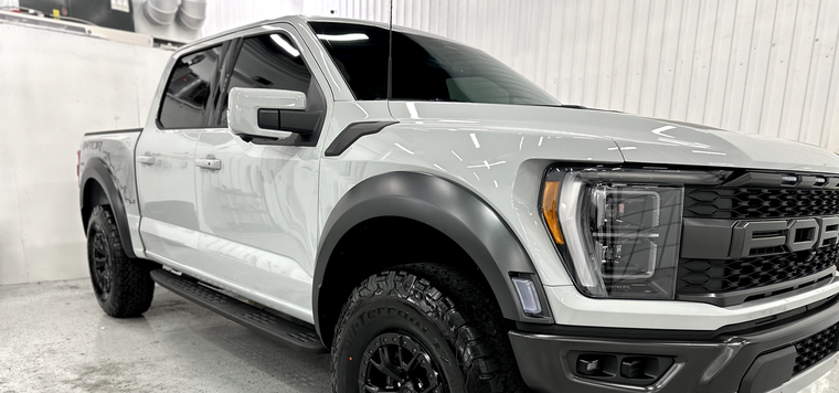 A white ford raptor truck is parked in a garage.