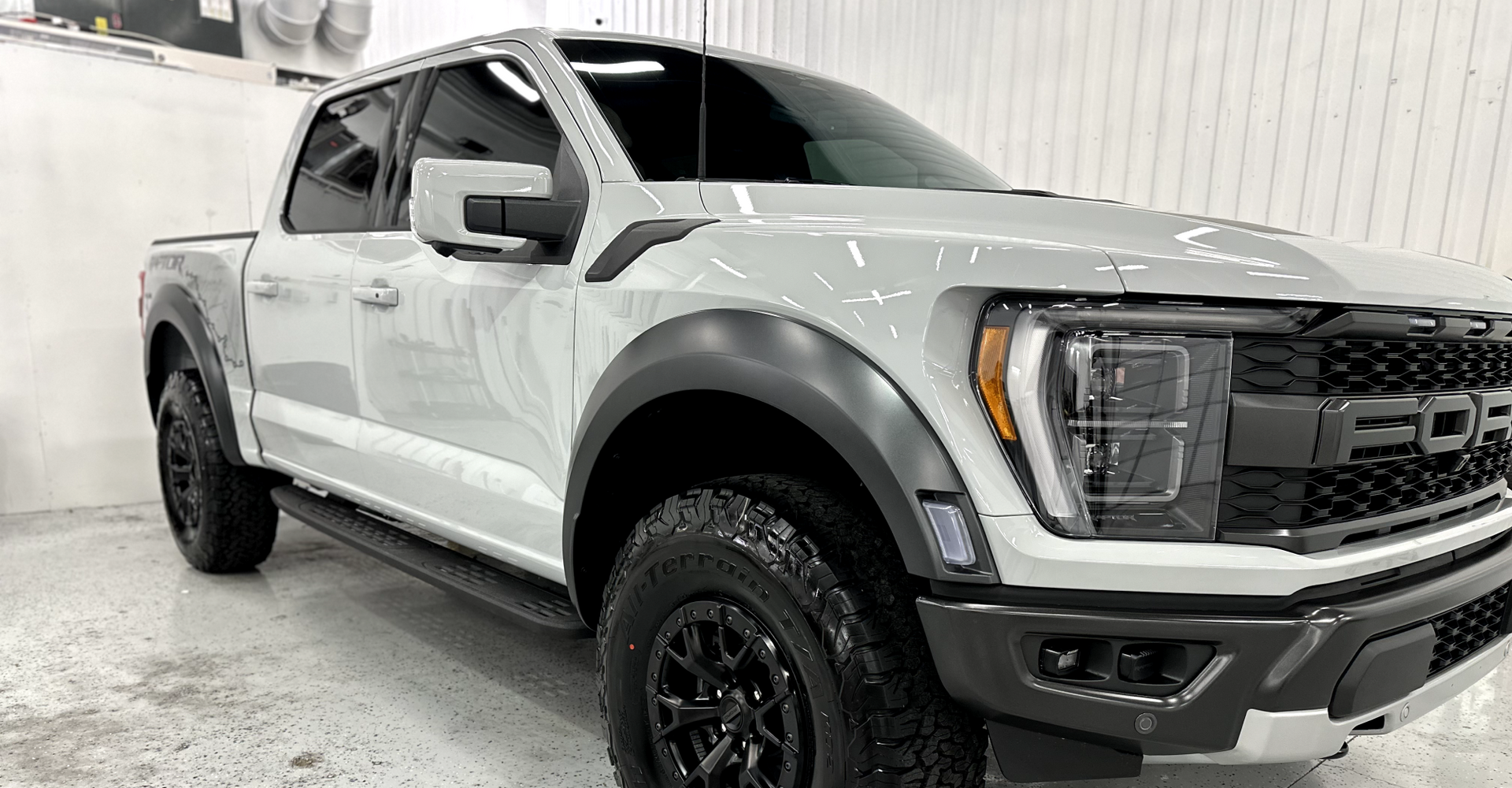 A white ford raptor truck is parked in a garage.