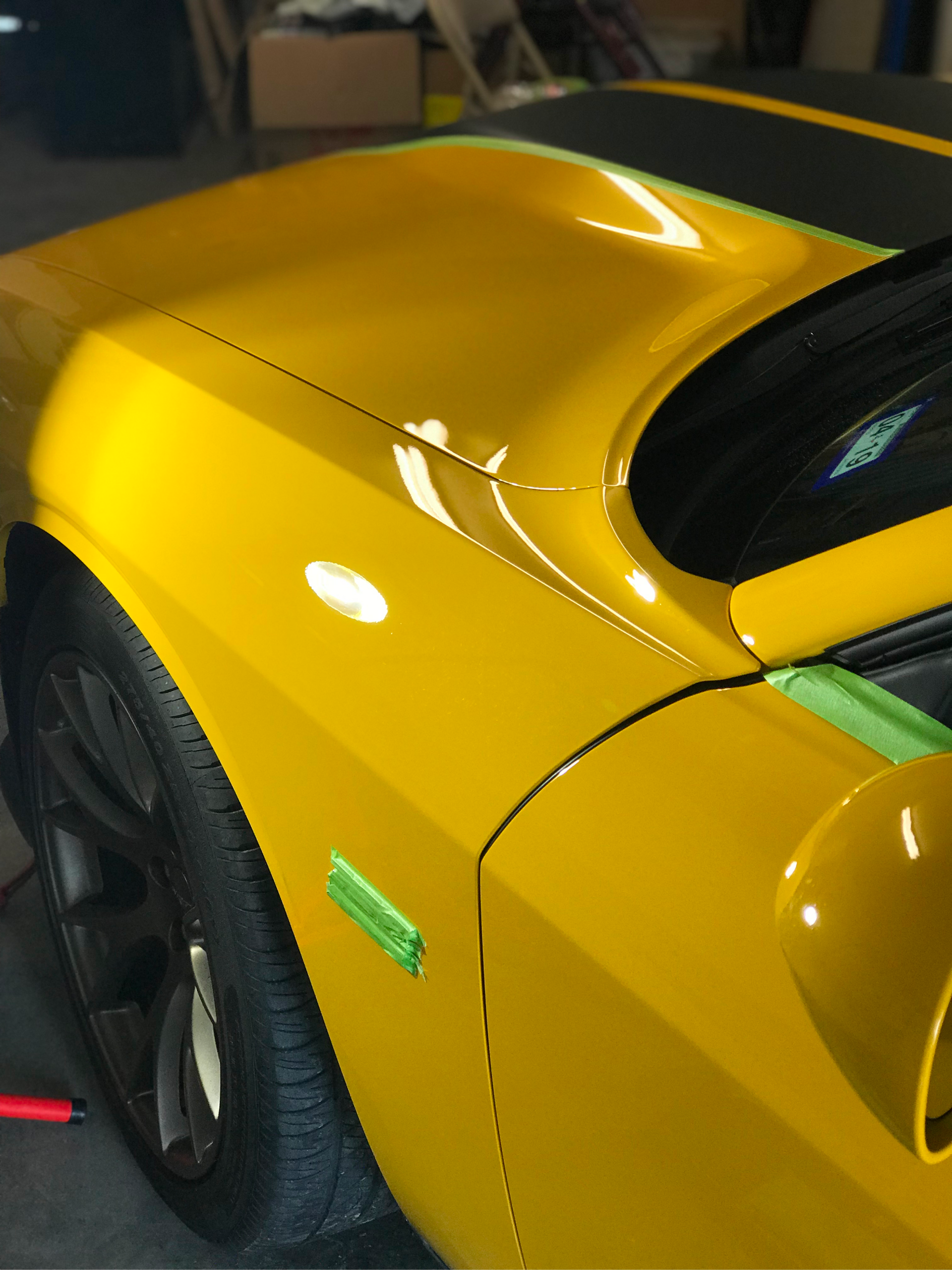 A yellow car with a black stripe on the hood