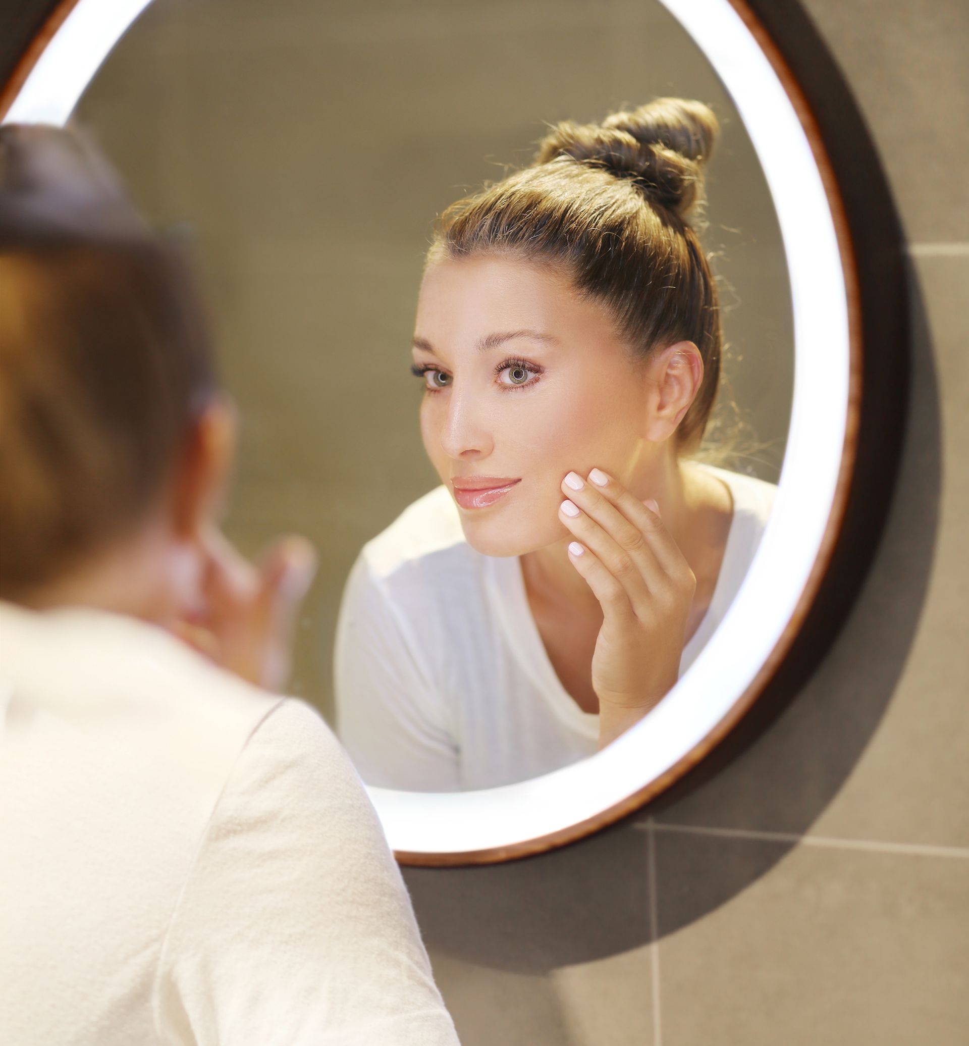 Woman examining skin in mirror, highlighting anti-aging and skincare services in Tuckahoe NY at Inner U Wellness