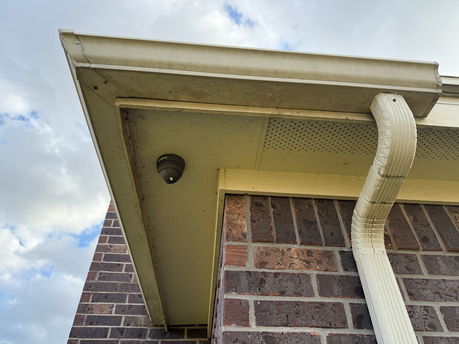 Security camera mounted under the roof overhang of a brick house near a gutter.