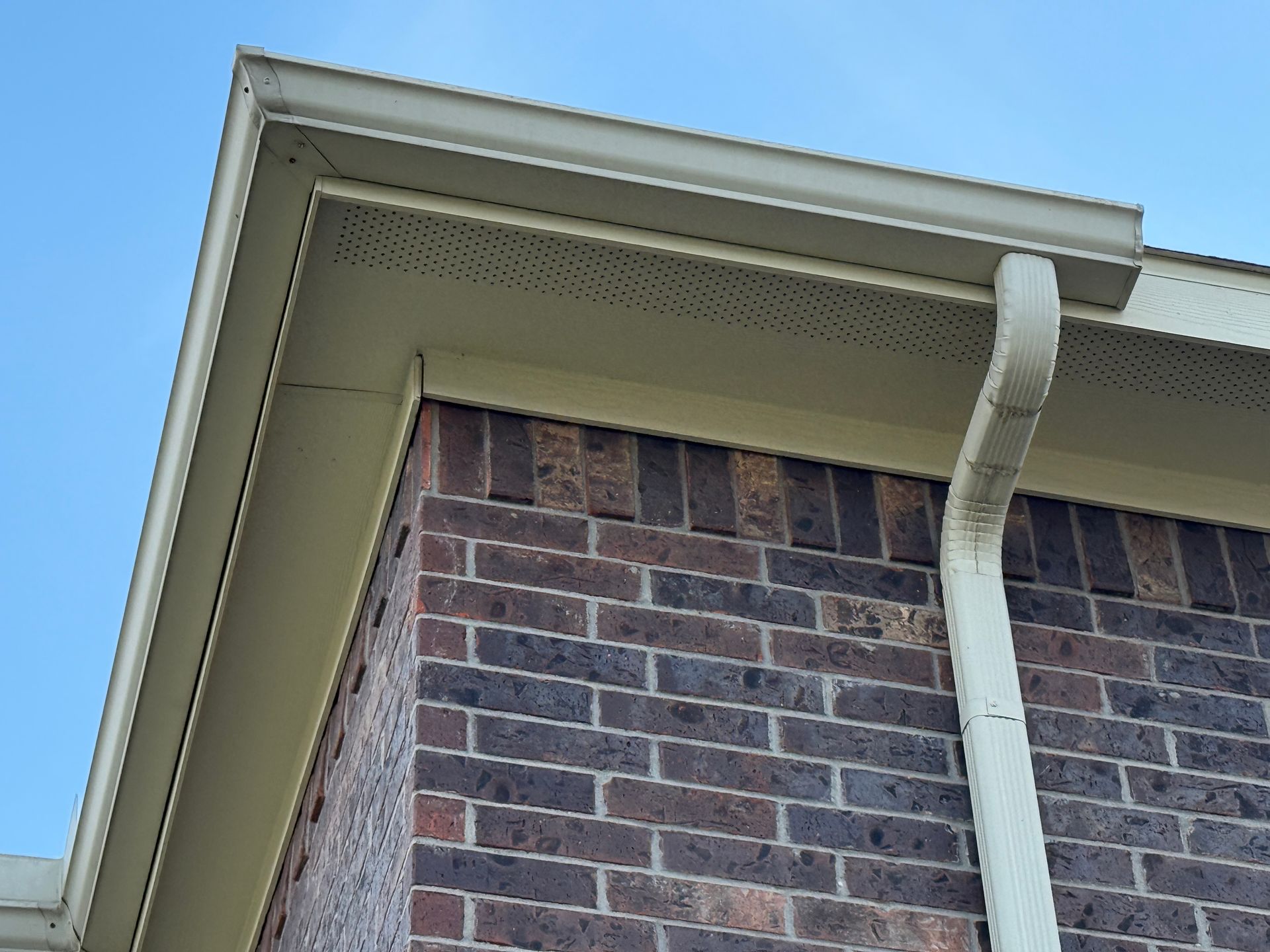 Tan gutters and soffit on a brick building corner against a blue sky.