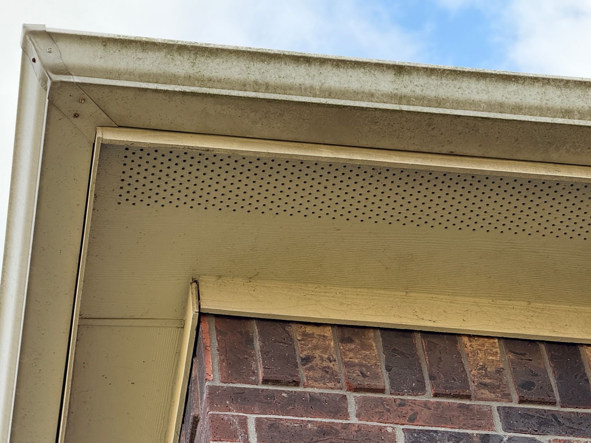 Beige house eaves and gutter, brick wall below.