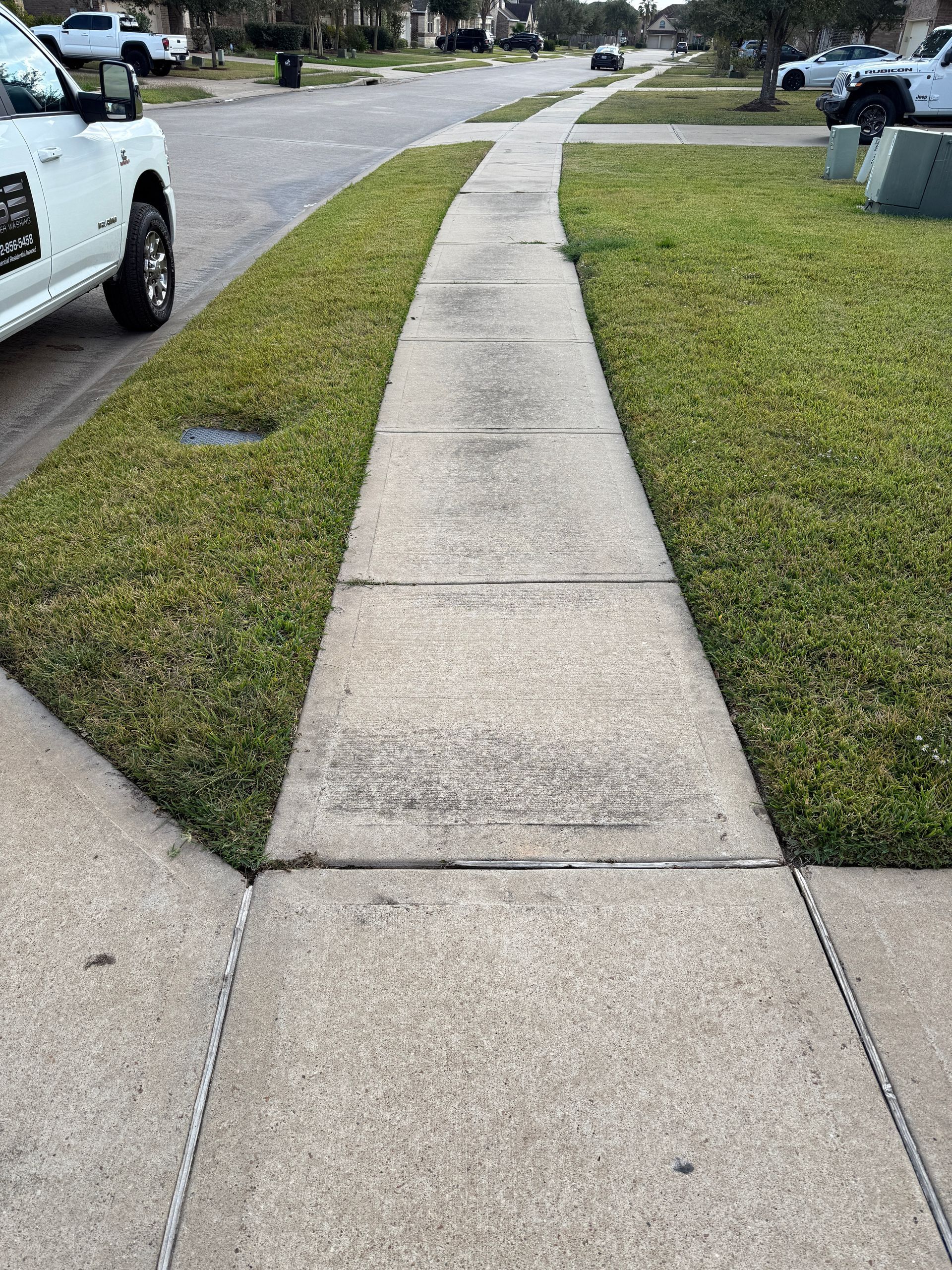 Concrete sidewalk bordered by grass, with a white truck parked on the street.