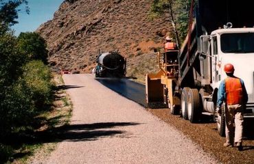 A man is walking down a road next to a dump truck.