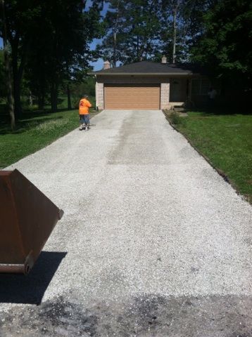 A man in an orange shirt is walking down a gravel driveway leading to a garage.