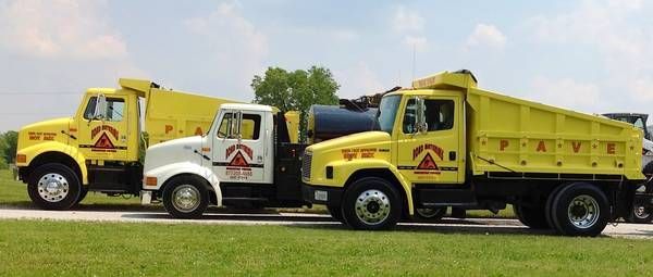 Two yellow dump trucks are parked next to each other in a grassy field.