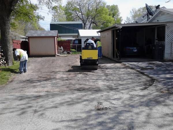A yellow truck is driving down a dirt road in front of a garage.