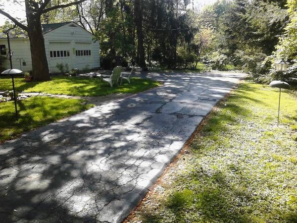 A driveway leading to a house surrounded by trees and grass