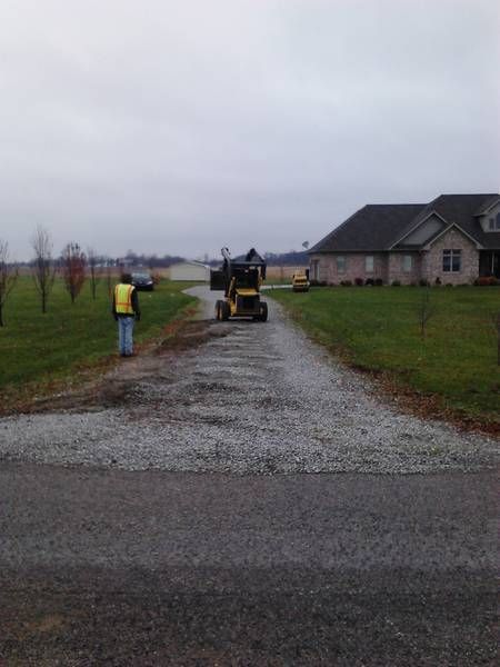 A man is walking down a gravel road in front of a house.