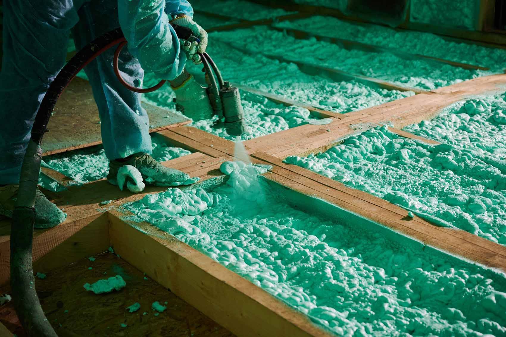 A man is spraying insulation on the floor of a house.