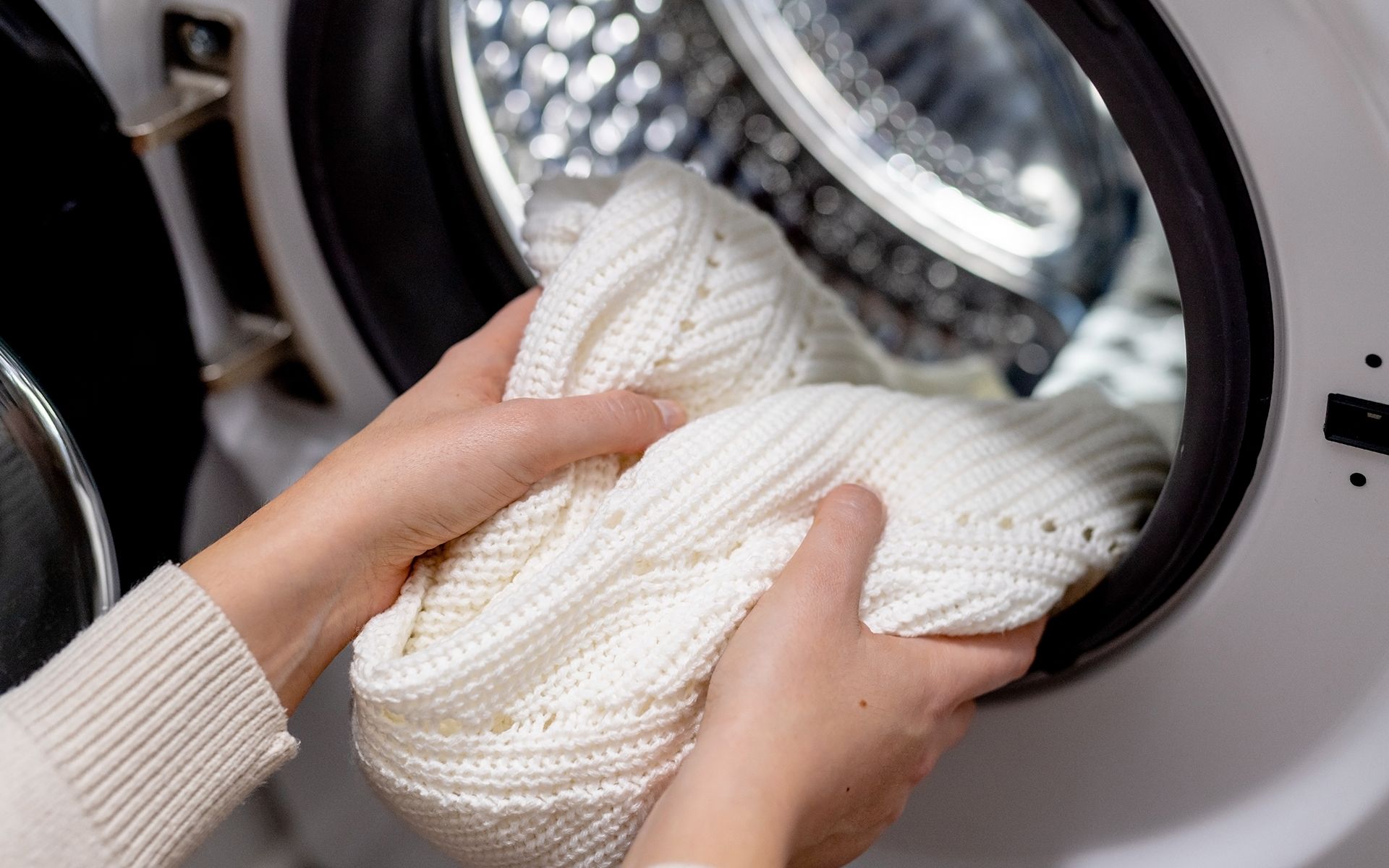 A person is putting a white sweater in a washing machine.