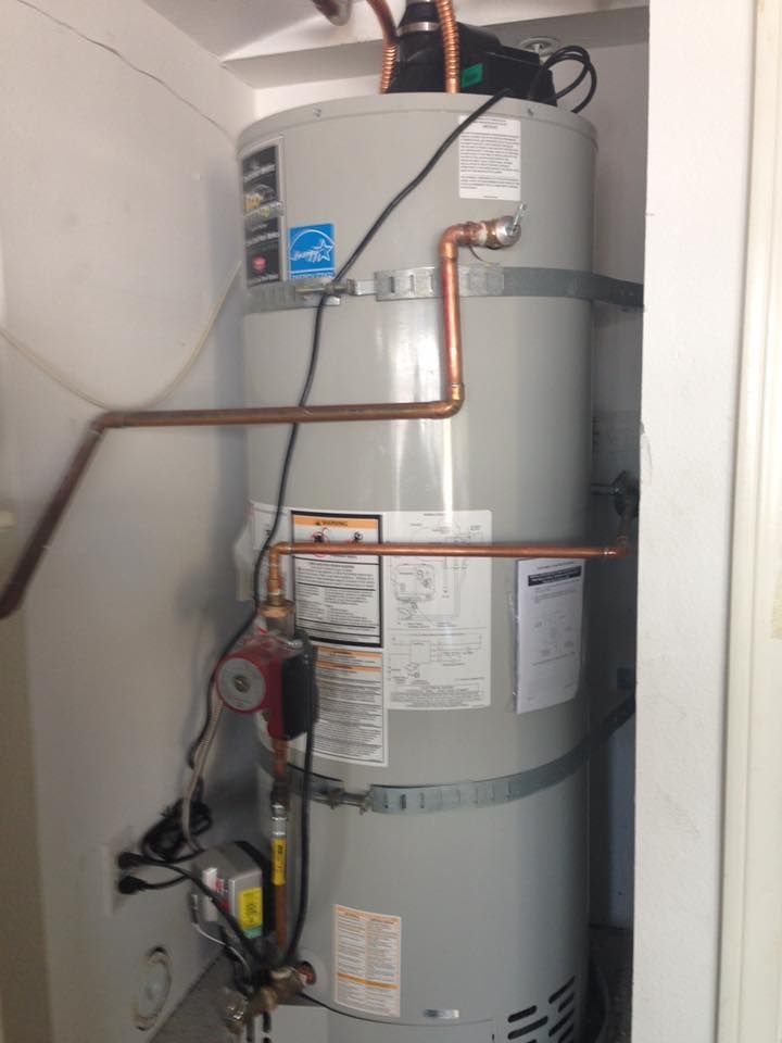 A grey water heater in a utility closet with copper piping, an attached red circulation pump, and electrical wiring.