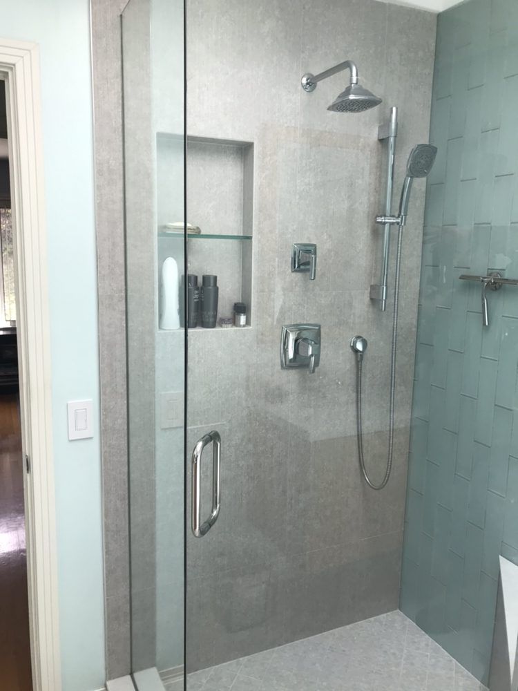 A modern walk-in shower with stone tile, a glass door, a built-in shelf, and a dual shower head system.