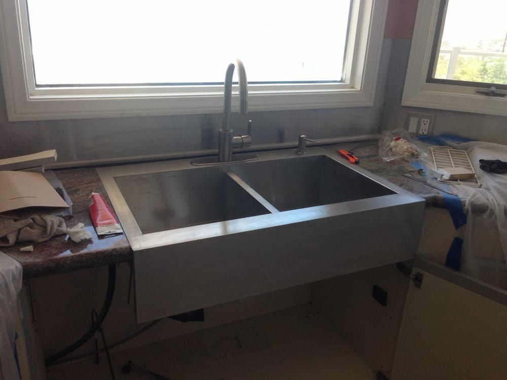 A stainless steel farmhouse kitchen sink installed in a counter under a window, with construction tools nearby.