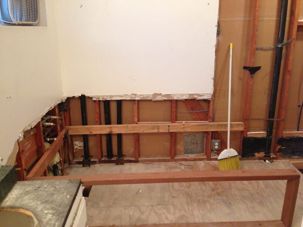 Exposed wood wall framing with pipes behind a sink, showing a home renovation in progress.