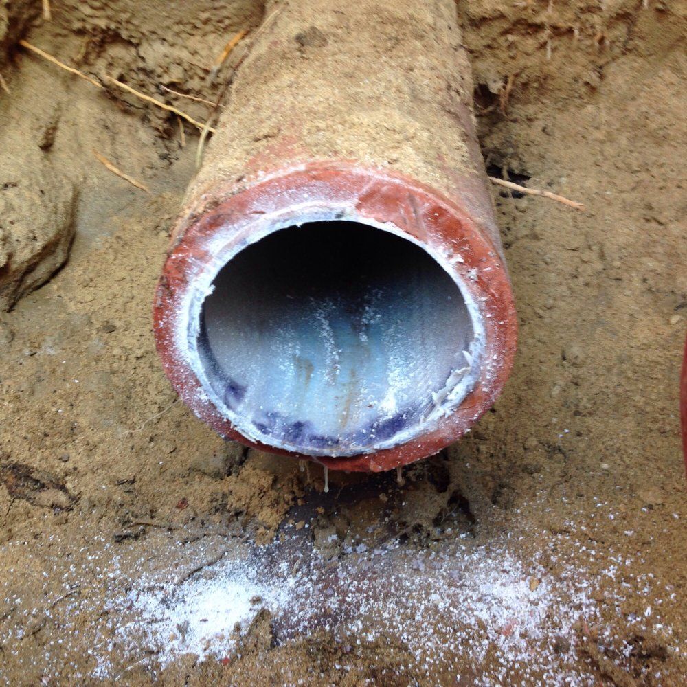 A red clay pipe in dirt with a white, crystalline substance residue on its opening and surrounding ground.