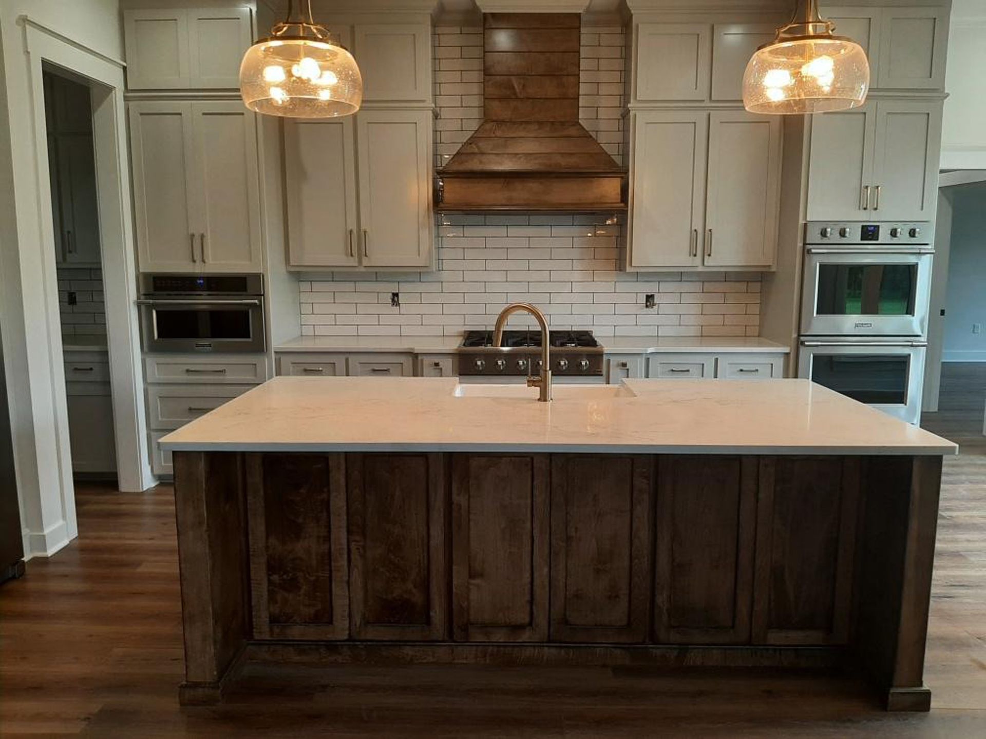 Kitchen with island, light cabinets, dark wood island and range hood, gold fixtures, white backsplash.