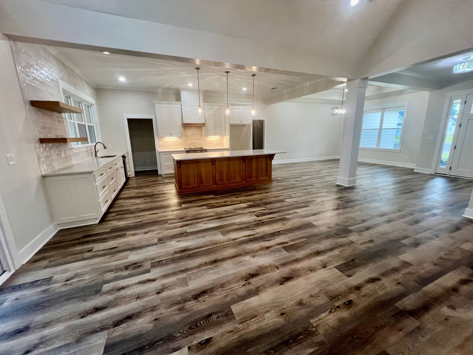 Open-concept kitchen with wooden island, white cabinets, and wood-look flooring.