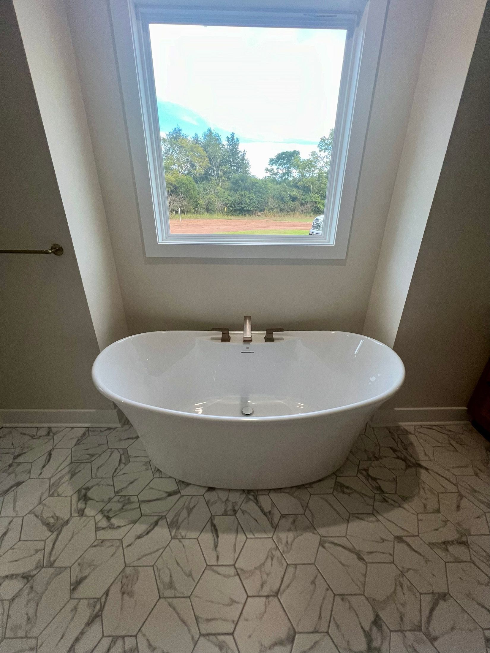 White freestanding bathtub in a bathroom, under a window with a view of greenery.
