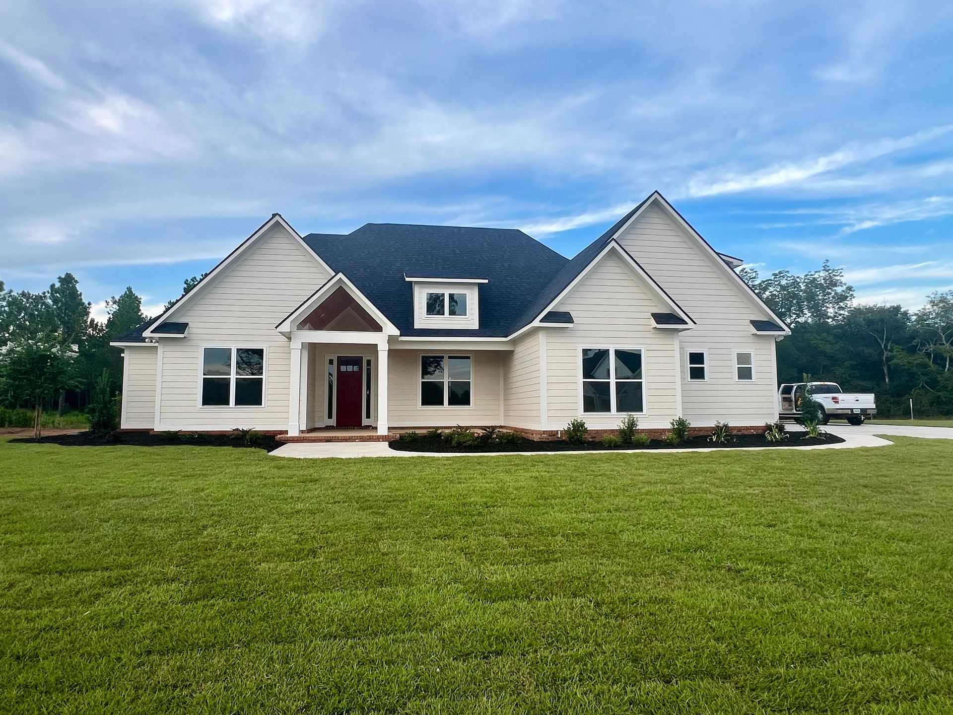 Cream-colored house with dark roof, red front door, and green lawn under a cloudy sky.
