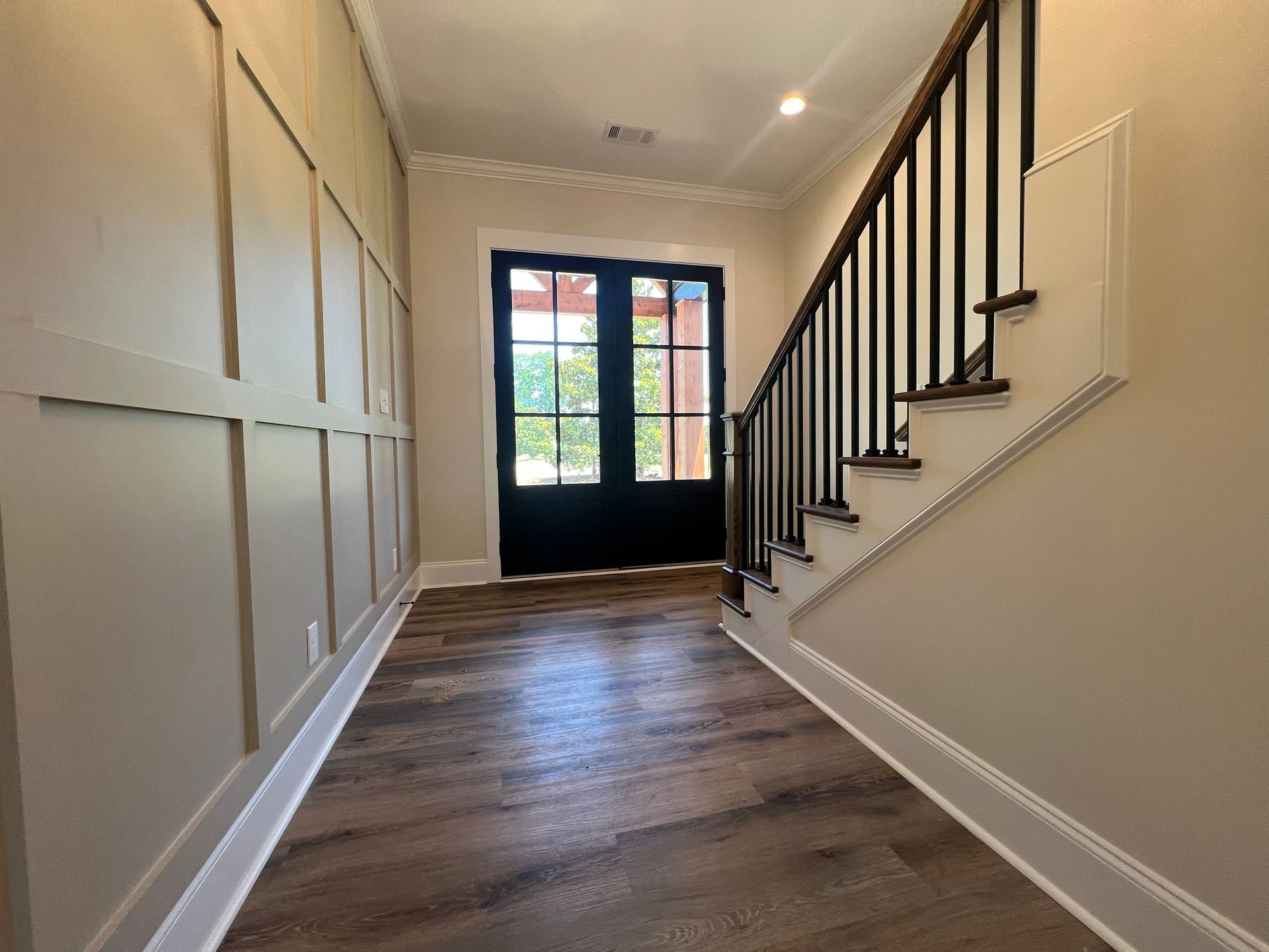 Entryway with wood floors, stairs, dark double doors, and beige paneling.