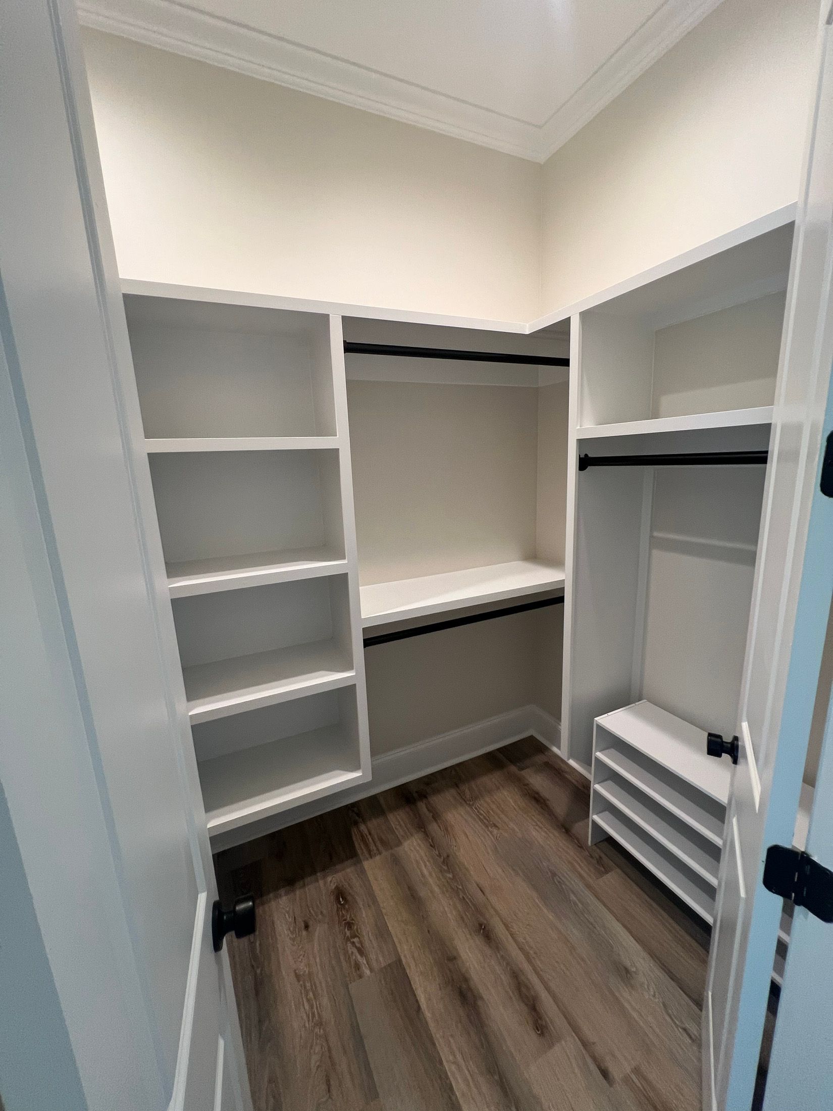 Walk-in closet with white shelves and rods, wood-look floor.